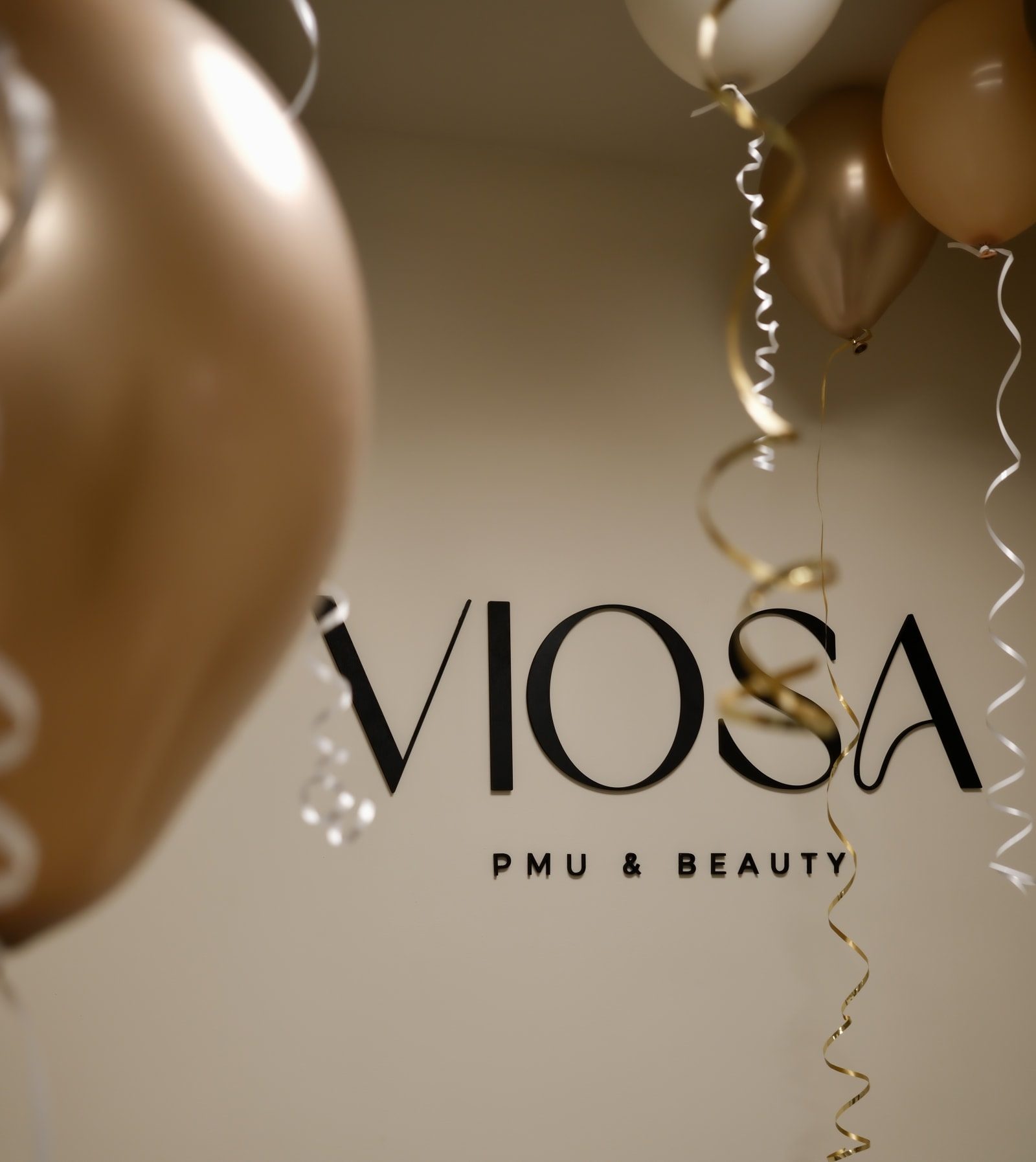 Het VIOSA logo op de muur met champagnekleurige ballonnen